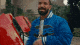 a man in a blue jacket is standing next to a red car and smiling .