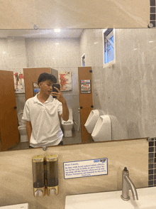 a man taking a picture of himself in a public restroom with a sign that says every drop