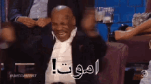 a man in a suit is sitting on a couch with his hands in his ears and a foreign language written on his face