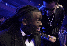 a man in a tuxedo with dreadlocks and a necklace with a cross on it