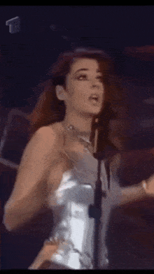 a woman in a silver dress is singing into a microphone on stage