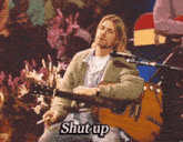 a man is smoking a cigarette while playing a guitar and the words shut up are visible