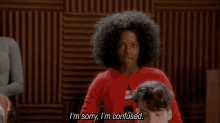 a woman with curly hair is sitting in front of a man and says i 'm sorry i 'm confused