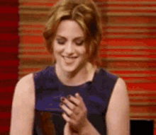a woman is smiling and clapping her hands in front of a red and white striped wall .
