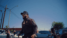 a man wearing sunglasses and a hat stands in front of cars