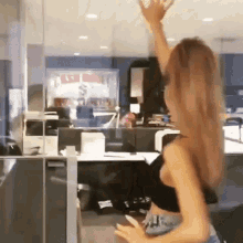 a woman in a black top is dancing in an office with her arms in the air .