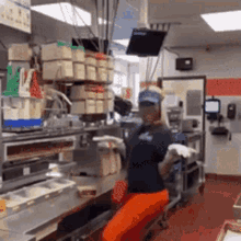 a woman in a blue shirt and orange pants is working in a kitchen .