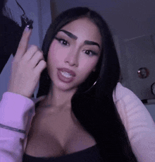a woman with long black hair is giving the middle finger while wearing a pink sweater .