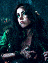 a woman with long dark hair is wearing a green top with feathers and a snake around her neck .