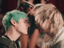a man with green hair and a man with blonde hair are looking at each other
