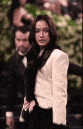 a woman in a white jacket stands in front of a man in a tuxedo