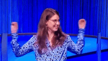 a woman wearing glasses and a blue shirt is raising her arms in the air .