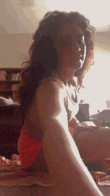 a woman with curly hair is sitting on a bed with her legs crossed