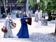 a man in a blue robe is carrying a box while a woman holds a bag