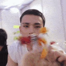 a man in a white shirt is holding a bouquet of flowers in front of his face .