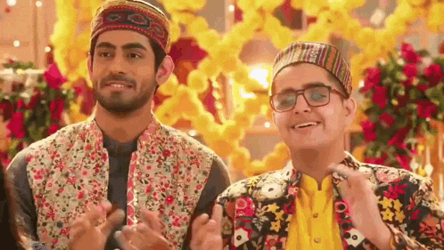 two men wearing hats and glasses are standing next to each other and clapping their hands .