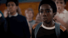 a boy with a backpack looks surprised in front of a crowd