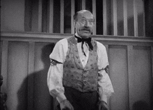 a black and white photo of a man in a vest and bow tie .