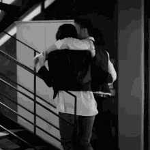 a black and white photo of a man carrying a woman on his back down a set of stairs .