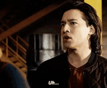 a man in a bomber jacket is talking to another man and says uh
