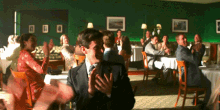 a man in a suit applauds while sitting in a restaurant