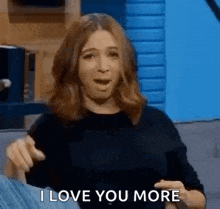 a woman is sitting on a couch with her mouth open and pointing at the camera while saying `` i love you more '' .