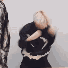 a man in a black sweater is standing in front of a white wall and dancing .