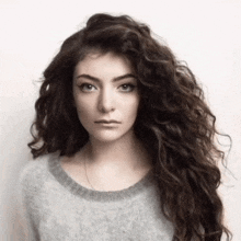 a woman with long curly hair is wearing a gray sweater