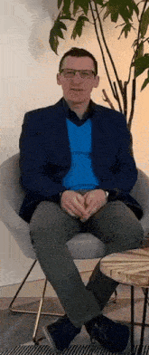 a man in a blue jacket is sitting in a chair with his legs crossed .