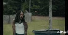 a man with dreadlocks is standing next to a trash can with imgplay written in the corner