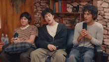 three men are sitting on a couch and one is holding a microphone in his hand