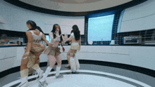 a group of women are dancing in a kitchen and one of them is wearing a plaid skirt