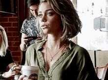 a woman is sitting at a table holding a cup of coffee and a cell phone .