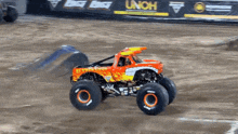 a monster truck is driving on a dirt track with a sign that says unoh in the background