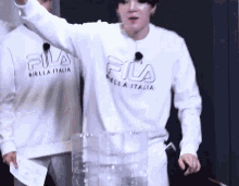 a man wearing a white fila sweatshirt is standing next to a stack of bottles .
