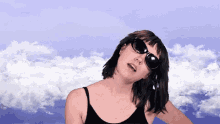 a woman wearing sunglasses stands in front of a cloudy sky
