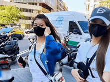 two women wearing face masks are standing in front of a van that says cb