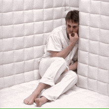 a man is sitting in a corner of a room with a white wall