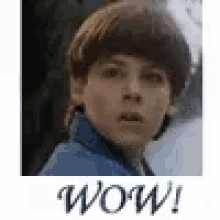 a young boy with a surprised look on his face is standing in front of a sign that says wow !