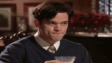 a man wearing a blue sweater and tie is holding a glass