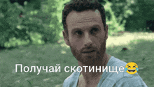 a man with a beard is standing in the grass with a smiley face behind him that says " получай скотинище "