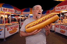 a man is holding a very long hot dog with mustard on it .