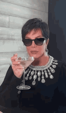 a woman wearing sunglasses is holding a martini in her hand .