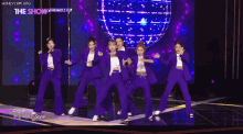 a group of women are dancing on a stage in purple suits .