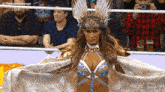 a woman in a costume with a crown on her head is standing in front of a crowd of people .