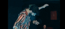 a man in a striped shirt is dancing with his arms outstretched .
