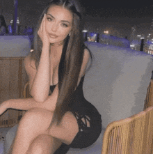 a woman in a black dress is sitting in a chair with her hand on her face .