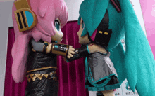 two mascots are hugging each other in front of a sign that says ' hatsune miku ' on it