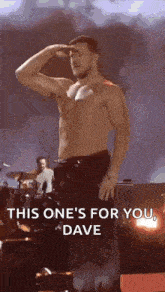 a shirtless man is saluting while standing on a stage with a drummer in the background .