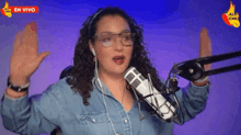 a woman wearing glasses and headphones stands in front of a microphone with her hands in the air .